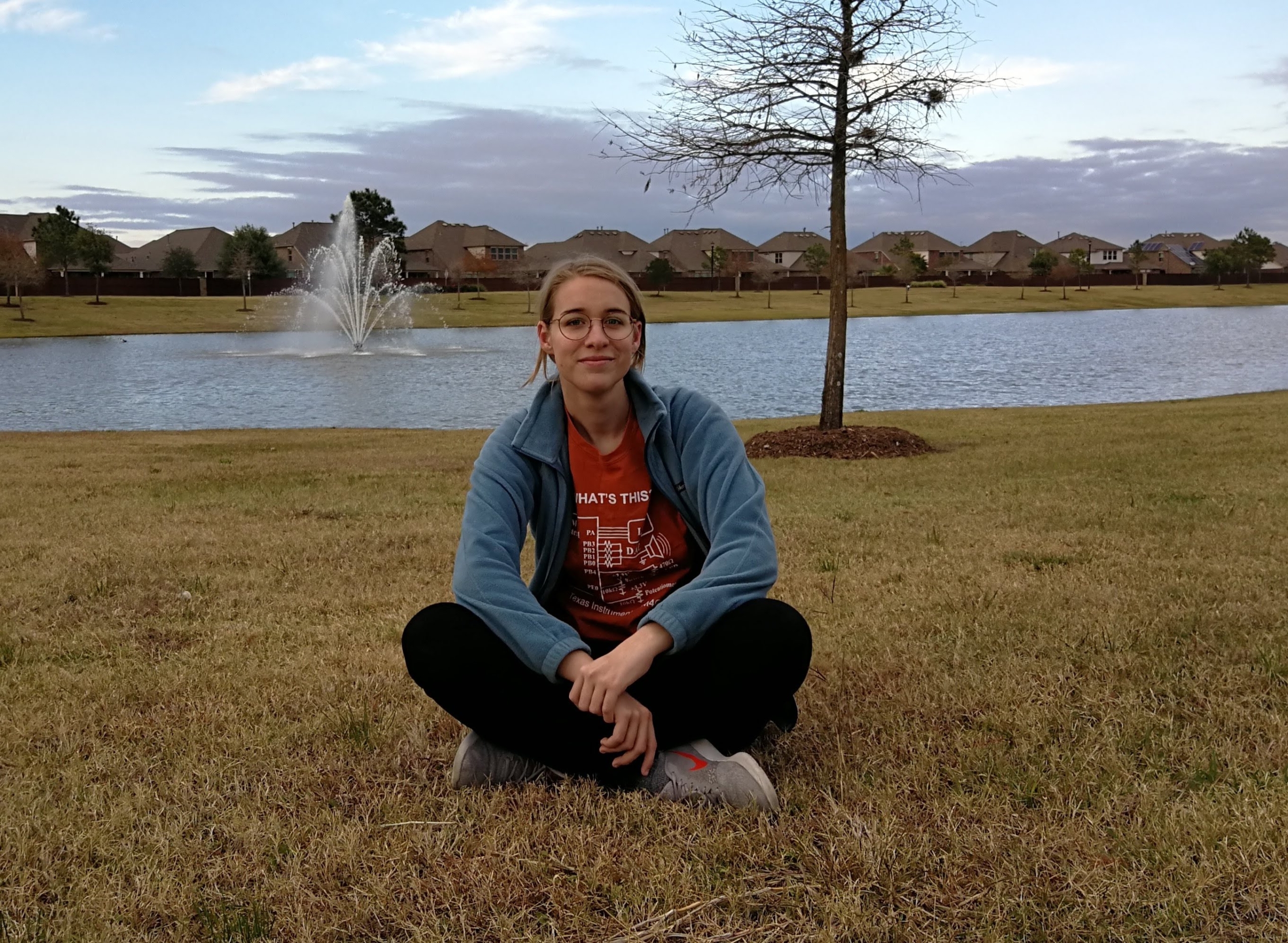 Profile image of Vivian Rogers, sitting on grass in front of a lake/fountain, full body.